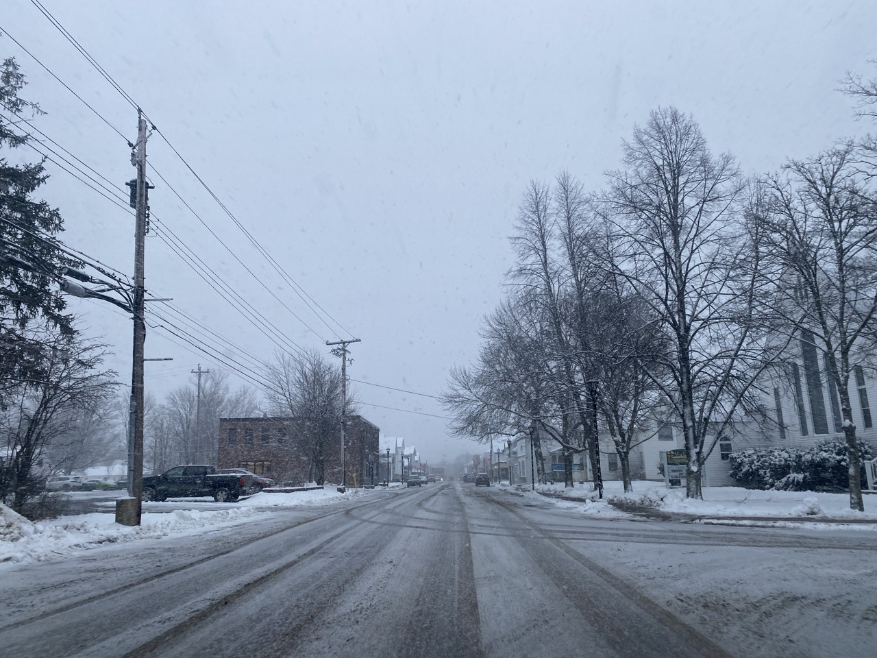 Snowy roads and white snowy sky. Small town Nova Scotia with power lines, bare snowy trees at the side and a few commercial buildings visible.