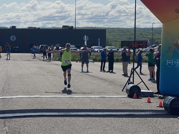 Male runner crossing the finish line of a race - people line the route in the background.